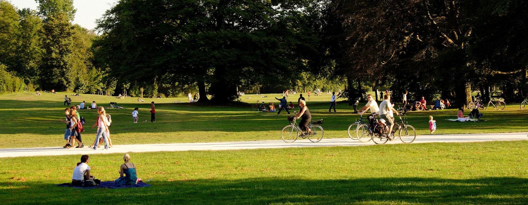A park with many people riding bikes, having a picnic, and walking.