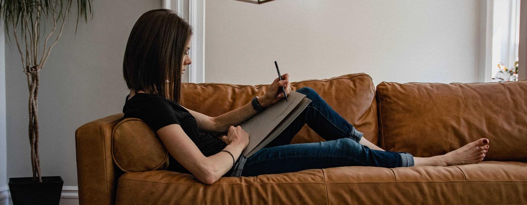 woman lies on a couch and draws on a large sketch pad